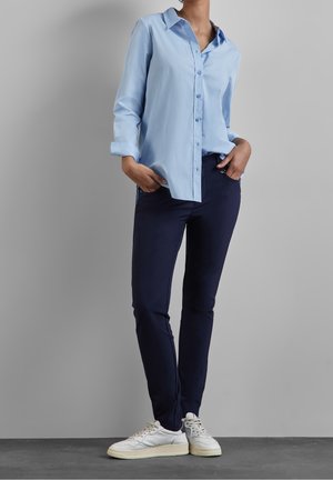 Camicia azzurro chiaro con bottoni, maniche lunghe. Pantaloni slim fit blu scuro. Sneakers bianche con dettagli grigi. Tessuto liscio, design casual.