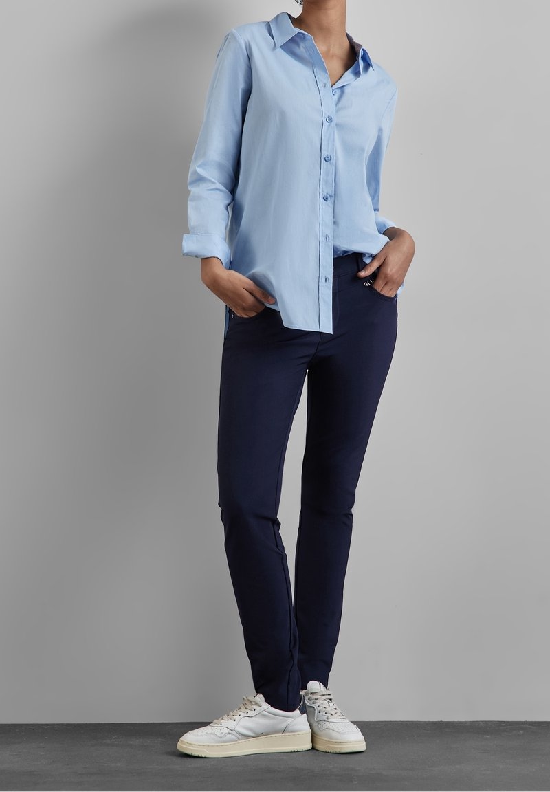 Chemise bleu clair à boutons, manches longues. Pantalon slim marine. Baskets blanches avec des accents gris. Tissu lisse, design décontracté.
