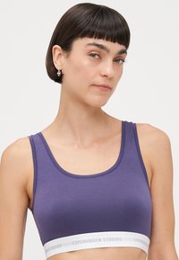 Lila pamut bralette, mély kivágással és vékony pántokkal. Fehér elasztikus szalaggal rendelkezik, amelyen a "COPENHAGEN STUDIOS" felirat látható. Simogató, sima felület.