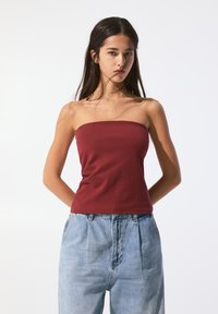 Top strapless burgundy din bumbac fin, cu un design ajustat, asociat cu pantaloni din denim de culoare albastru deschis, cu talie înaltă și pliseuri.