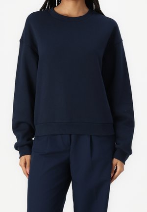 Mørkeblå sweatshirt i blødt bomuldsmateriale med rund halsudskæring, afslappet pasform og ribstrikkede ærmeender. Kombineret med matchende mørkeblå bukser.
