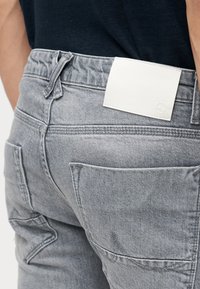 Κοντινό πλάνο στο πίσω μέρος προσώπου που φοράει ανοιχτό γκρι τζιν παντελόνι με μεγάλες πίσω τσέπες και λευκό δερμάτινο σημάδι στη μέση.