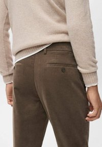 Pantalones de pana marrón con dos bolsillos traseros y cierres de botón, combinados con un suéter de color beige claro que presenta un puño acanalado.