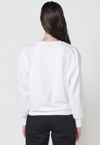 Felpa bianca con maniche lunghe, polsini e orlo a coste. Texture liscia con una vestibilità comoda. Nessun motivo visibile o dettagli hardware.