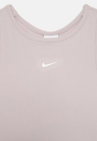 Lyserosa ribbet tanktopp med rund hals og en liten hvit Nike-logo sentrert på brystet. Myk stofftekstur.
