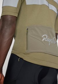 Maillot de cyclisme vert olive en tissu texturé avec des panneaux en maille. Comprend une poche zippée et un détail de logo réfléchissant.
