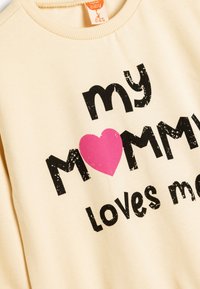 Lichtbeige sweatshirt met grote zwarte tekst die zegt "mijn MAMA houdt van me" met een grote roze hartaccent in het midden.