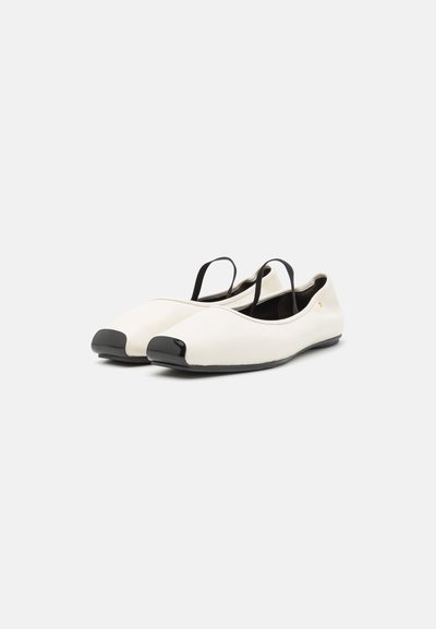 Hvide balletflade sko med en blank sort tåhætte, tynde sorte stropper og en blød læderoverflade. Minimalistisk design med en let kurve.