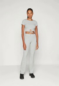 Sivi kratki top s čvorom na sredini, uparen s odgovarajućim sivim širokim hlačama. Tkanina se čini mekom s glatkom teksturom.