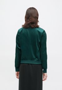 Green satin bomber jacket with a ribbed hem and cuffs, featuring a smooth texture and an aerodynamic fit, shown from the back.