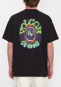 Sort bomulds t-shirt med et farverigt grafikdesign af en mund og teksten "VOLCOM STONE" i levende grøn og pink.