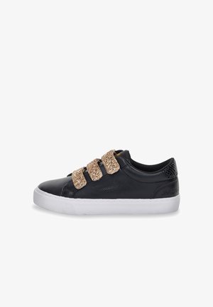 Zapatilla deportiva de cuero negro con tres correas doradas brillantes y suela de goma blanca. Cuenta con un detalle texturizado negro en el talón.