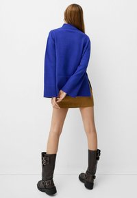 Blue knitted sweater with a high collar and ribbed cuffs, paired with a brown suede mini skirt and knee-high buckled boots.