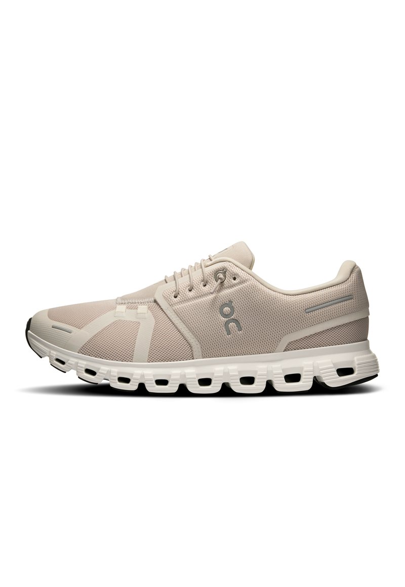Light beige athletic shoes with a mesh upper, secure lacing, a cushioned sole, and distinctive cut-out design on the outsole for flexibility.