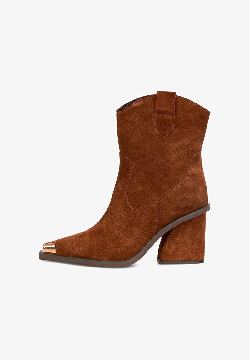 Botín de ante marrón con punta cuadrada, adornado con una tapa de metal dorado y un tacón grueso. Presenta detalles de costura y una lengüeta.