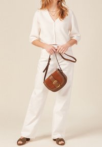 Cardigan bianco a maniche corte con bottoni, abbinato a pantaloni bianchi a vita alta. Borsa a tracolla in pelle marrone con dettaglio a fibbia. Sandali verde oliva.