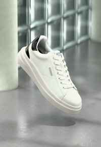 Weiße Leder-Sneaker mit schwarzen Akzenten, runder Zehenpartie, dicker Sohle und Markenaufdruck an der Zunge. Verfügt über weiße Schnürsenkel und eine glatte, glänzende Textur.