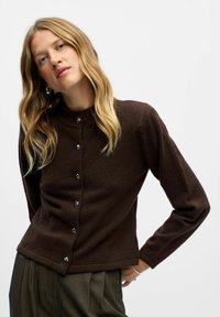 Cardigan en tricot marron avec un col montant, présentant une rangée de boutons en argent sur le devant et des manches longues. Tissu texturé, coupe décontractée.