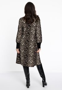 Leopardenmuster-Kleid mit langen puffigen Ärmeln, schwarzen Manschetten und einem ausgestellt geschnittenen Saum. Getragen mit kniehohen schwarzen Stiefeln.
