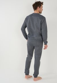 Sudadera de felpa gris y joggers a juego, ambos con puños acanalados y una textura cepillada, mostrados desde la parte de atrás con los pies descalzos.