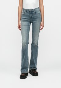 Vaqueros acampanados de denim azul claro con un acabado desgastado, cinco bolsillos y una cintura con pasadores para cinturón, combinados con zapatos de plataforma negros y gruesos.