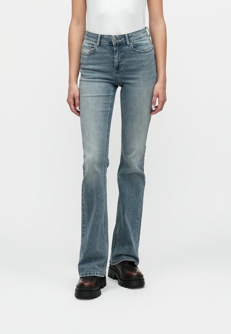 Vaqueros acampanados de denim azul claro con un acabado desgastado, cinco bolsillos y una cintura con pasadores para cinturón, combinados con zapatos de plataforma negros y gruesos.