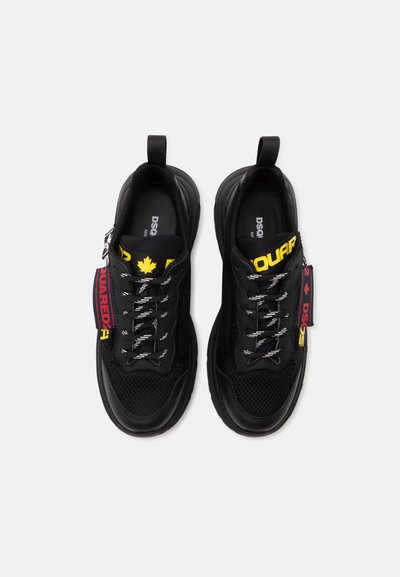 Baskets noires avec détails en mesh et cuir, lacets blancs à motifs, logo jaune DSQUARED2 sur les languettes, et étiquettes rouges de marque sur les côtés.