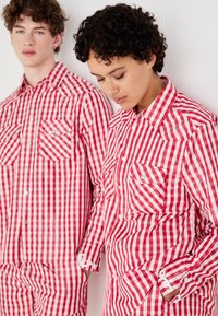 Rot-weiße Karomusterhemden mit Brusttaschen, Button-Down-Kragen und langen Ärmeln, präsentiert von zwei Personen, die nebeneinander stehen.
