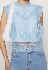 Ljusblå spetstopp med vågiga ärmar, intrikata mönster och en dekorativ nederdel. Matchad med ljusblå denimjeans.