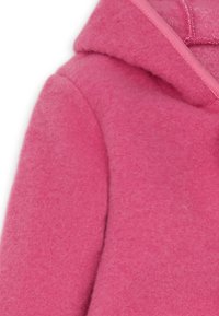 Roze fleecejack met een capuchon, met een gestructureerd oppervlak en contrasterende bies langs de rand. Close-up van het schoudergebied.