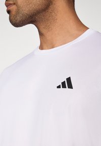 T-shirt atlética branca com acabamento texturizado e detalhe em preto com três formas triangulares pretas na área do peito.