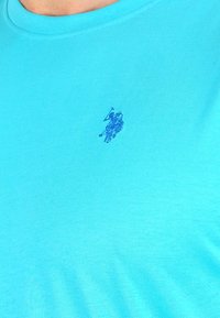 Turkizna bombažna majica s kratkimi rokavi in okroglim izrezom; ima majhen modro izvezen konjski logo na levi strani prsnega koša.