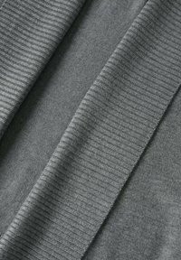 Tissu gris avec textures en tricot lisse et côtelé, plié pour montrer le contraste entre les motifs plats et côtelés.