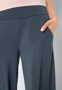Pantaloni larghi grigio scuro con una texture liscia, vita elastica e tasche laterali. Le tasche sono posizionate sui fianchi.