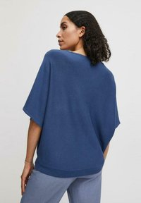 Top de punto azul con un estilo suelto y mangas de murciélago, y un escote ancho. Cuenta con mangas cortas y un dobladillo acanalado. Textura suave y ajuste relajado.