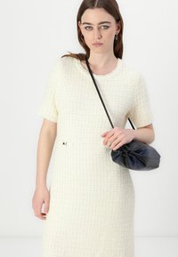 Robe tricotée crème avec un motif en grille texturé et des manches courtes. Accentuée d'un petit fermoir en or ; associée à un sac pochette noir.