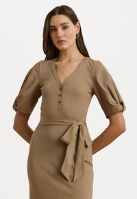 Abito beige a costine con scollatura a V, maniche corte a palloncino e bottoni. Presenta un dettaglio in vita da annodare per una silhouette aderente.