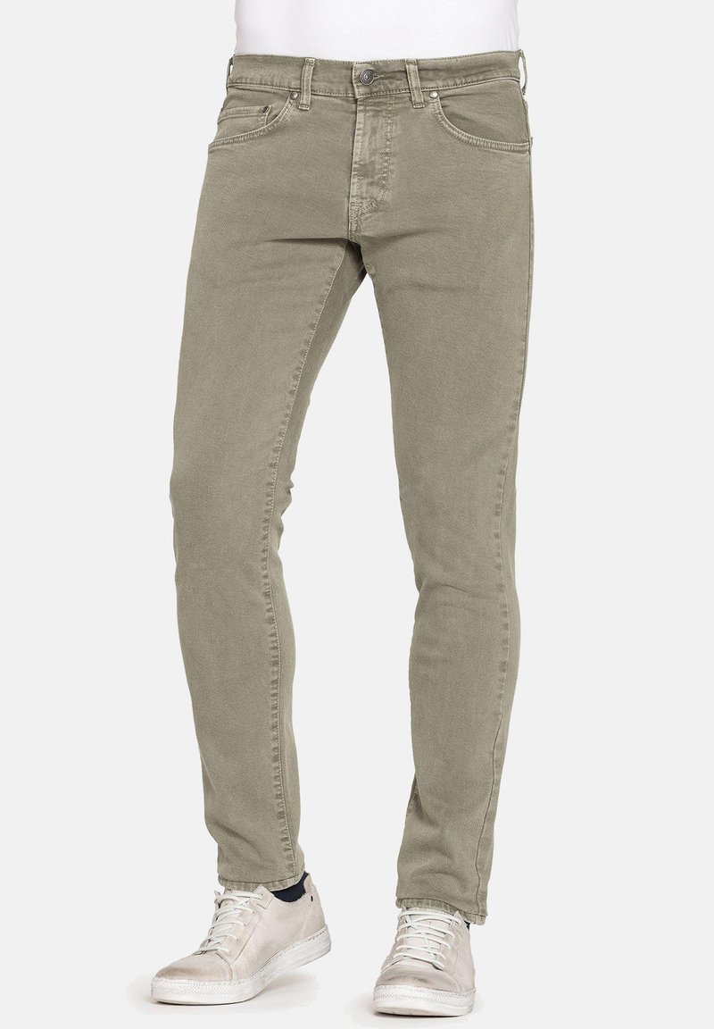 Jeans slim-fit verde oliva realizzati in cotone con una texture liscia, dotati di tasche standard e chiusura con zip. Abbinati a sneakers bianche.