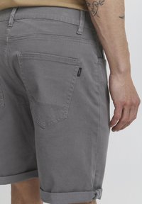 Gray denim shorts with rolled cuffs, five-pocket design, and a small tag detail on the back pocket. Smooth texture, casual style.