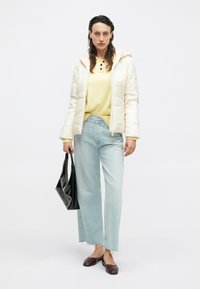 Giacca crema trapuntata, maglione giallo, jeans a gamba larga blu chiaro con orlo scucito, borsa nera, scarpe marroni, stile casual, design minimalista.