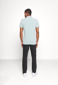 Polo de color verde claro con mangas cortas, combinado con pantalones negros y zapatillas blancas. La tela parece suave con un corte clásico.