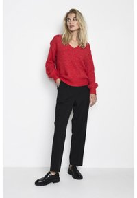 Roter, strukturierten V-Ausschnitt-Pullover kombiniert mit schwarzen, taillierten Hosen und glänzenden schwarzen Mokassins. Schlichtes, modernes Design mit lässiger Passform.