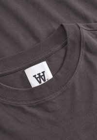 Graues Baumwoll-T-Shirt mit rundem Ausschnitt, subtiler Textur und einem Etikett mit einem stilisierten Logo am Hals.