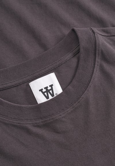 T-shirt in cotone grigio con collo rotondo, texture sottile e un'etichetta con un logo stilizzato sul collo.