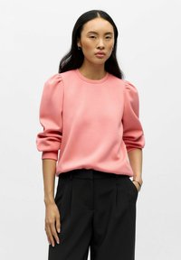 Roze sweatshirt met opgestoken mouwen, ronde hals en zachte textuur, gecombineerd met zwarte op maat gemaakte broek. Eenvoudig ontwerp zonder zichtbare patronen.