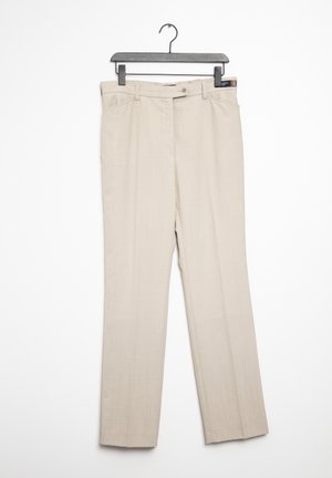 Pantalones beige a medida con trabillas para cinturón, botón frontal y cremallera, colgados en una percha de plástico negra sobre un fondo blanco.