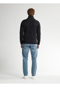 Mörk stickad tröja med hög krage, texturerad ribbning vid axlarna, ihop med ljusblå jeans och vita sneakers.