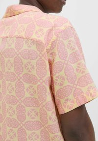 Kurzärmliges Hemd in hellgelb mit pinken Blumen- und Ovalmustern. Weiche Textur mit lässigem Schnitt und klassischem Kragendesign.