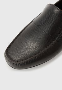 Mocasini din piele neagră cu o suprafață texturată, cusături detaliate, vârf rotunjit și guler ușor ridicat. Fără hardware vizibil.