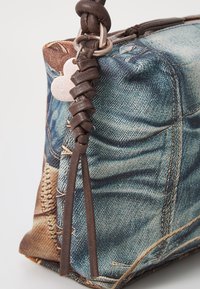 Sac à motif denim avec accents en cuir ; doté d'une sangle tressée et d'un charm en forme de cœur en métal sur la fermeture éclair. Surface en tissu texturé.